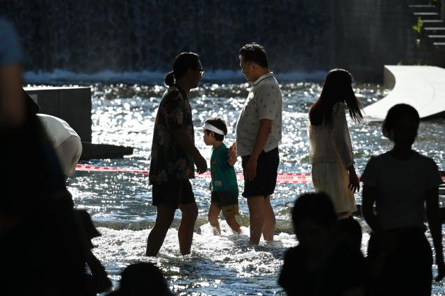People walk through the Cheonggyecheon Stream to cool off in Seoul on August 2, 2026. South Korea registered its highest temperature since records began more than a century ago on August 2, as authorities warned people to "immediately" stop all outdoor activities in affected areas. (Photo by GREG BAKER / AFP)