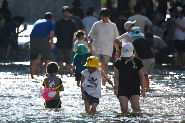 People walk in the Cheonggyecheon Stream to cool off in Seoul on August 2, 2026. South Korea registered its highest temperature since records began more than a century ago on August 2, as authorities warned people to "immediately" stop all outdoor activities in affected areas. (Photo by GREG BAKER / AFP)