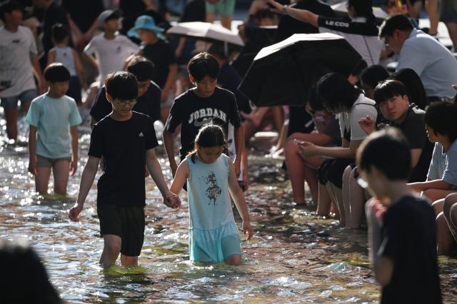 Children walk through the Cheonggyecheon Stream to cool off in Seoul on August 2, 2026. South Korea registered its highest temperature since records began more than a century ago on August 2, as authorities warned people to "immediately" stop all outdoor activities in affected areas. (Photo by GREG BAKER / AFP)