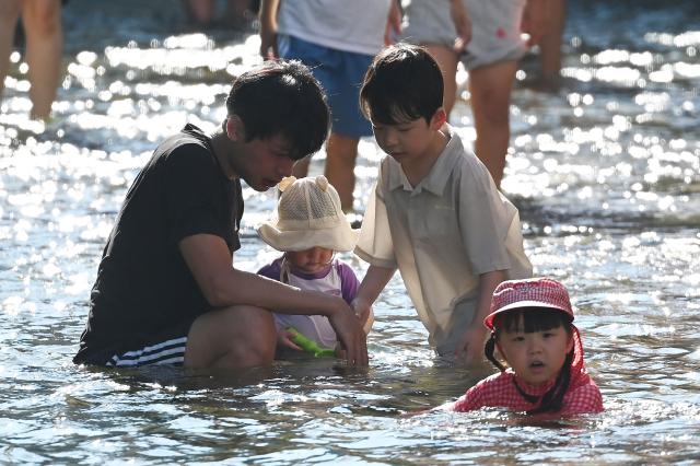 A family plays in the Cheonggyecheon Stream to cool off in Seoul on August 2, 2026. South Korea registered its highest temperature since records began more than a century ago on August 2, as authorities warned people to "immediately" stop all outdoor activities in affected areas. (Photo by GREG BAKER / AFP)