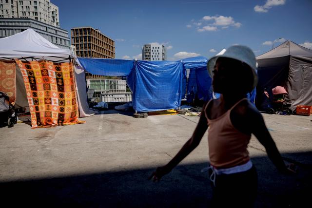A child walks past makeshift tents in the forecourt of the Samusocial headquarters of the Samusocial headquarters, occupied by families and people waiting for emergency accommodation, in Paris, France, on August 1, 2026. The CGT union branch of the Paris Samusocial announced the continuation of a strike launched on June 23, in its sixth week, protesting against what it described as "the return of too many families to the streets". Utopia 56, an association that supports migrants and homeless people, has been occupying the forecourt of the Samu social headquarters in Paris for a week in support of the families. “There are nearly 200 people” on site, waiting for housing, according to the CGT. (Photo by Simon WOHLFAHRT / AFP)