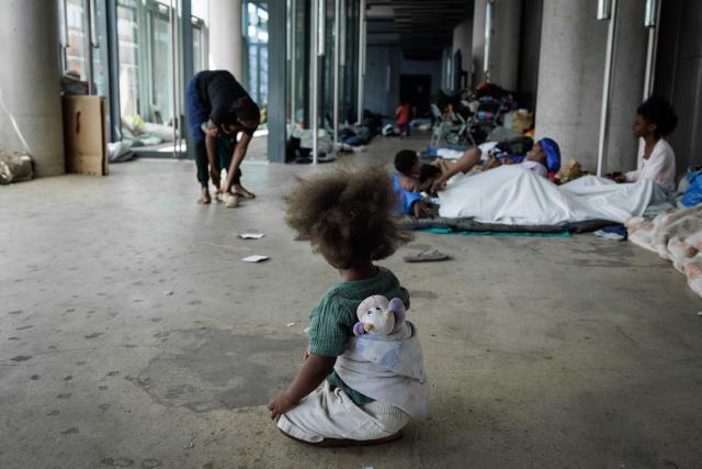 A child sits next to people resting inside the Samusocial headquarters, occupied by families and people waiting for emergency accommodation, in Paris, on August 1, 2026. The CGT union branch of the Paris Samusocial announced the continuation of a strike launched on June 23, in its sixth week, protesting against what it described as "the return of too many families to the streets". Utopia 56, an association that supports migrants and homeless people, has been occupying the forecourt of the Samu social headquarters in Paris for a week in support of the families. “There are nearly 200 people” on site, waiting for housing, according to the CGT. (Photo by Simon WOHLFAHRT / AFP)