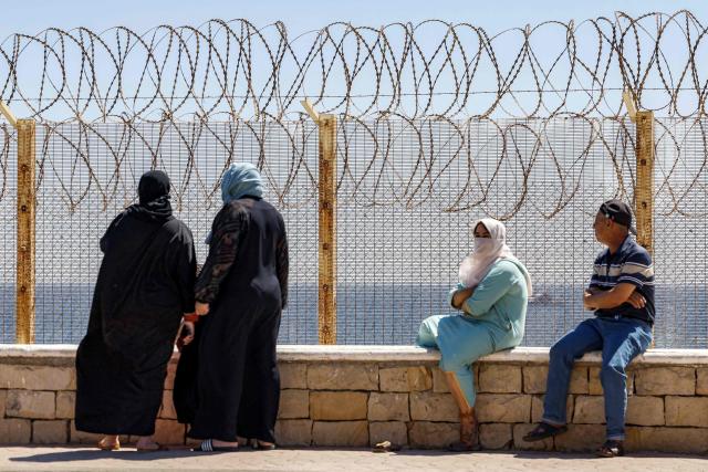 Relatives and friends wait by a fence topped with barbed-wire for the return of people who had previously crossed into Spain's North African enclave of Ceuta, at Morocca's Bab Sebta border crossing on the outskirts of Fnideq on August 2, 2026. As many as 60,000 migrants entered Ceuta in recent days, mostly swimming around the small border post that juts into the Mediterranean Sea, in an unprecedented surge that prompted an international crisis for Spain. The mass crossing into the tiny Spanish territory resulted in at least 67 deaths, according to Spanish authorities, and led to clashes with Moroccan police on the shared border. (Photo by Abdel Majid BZIOUAT / AFP)