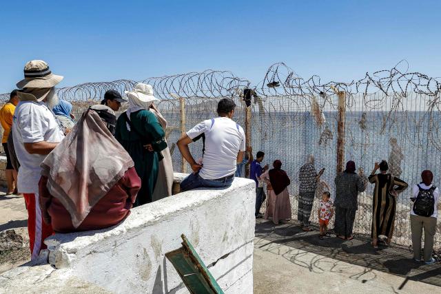 Relatives and friends wait by a fence topped with barbed-wire for the return of people who had previously crossed into Spain's North African enclave of Ceuta, at Morocca's Bab Sebta border crossing on the outskirts of Fnideq on August 2, 2026. As many as 60,000 migrants entered Ceuta in recent days, mostly swimming around the small border post that juts into the Mediterranean Sea, in an unprecedented surge that prompted an international crisis for Spain. The mass crossing into the tiny Spanish territory resulted in at least 67 deaths, according to Spanish authorities, and led to clashes with Moroccan police on the shared border. (Photo by Abdel Majid BZIOUAT / AFP)