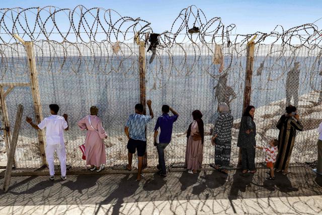 Relatives and friends wait by a fence topped with barbed-wire for the return of people who had previously crossed into Spain's North African enclave of Ceuta, at Morocca's Bab Sebta border crossing on the outskirts of Fnideq on August 2, 2026. As many as 60,000 migrants entered Ceuta in recent days, mostly swimming around the small border post that juts into the Mediterranean Sea, in an unprecedented surge that prompted an international crisis for Spain. The mass crossing into the tiny Spanish territory resulted in at least 67 deaths, according to Spanish authorities, and led to clashes with Moroccan police on the shared border. (Photo by Abdel Majid BZIOUAT / AFP)