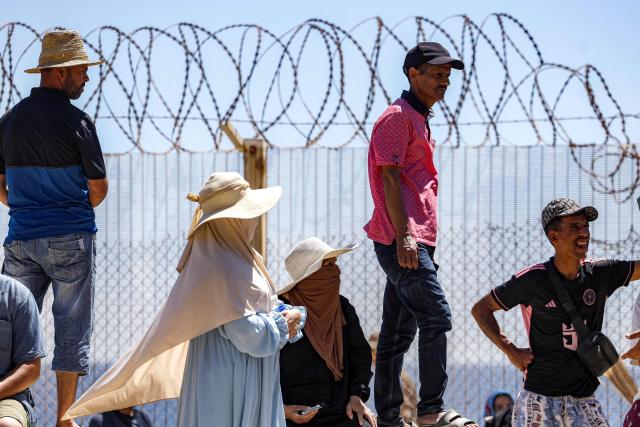 Relatives and friends wait by a fence topped with barbed-wire for the return of people who had previously crossed into Spain's North African enclave of Ceuta, at Morocca's Bab Sebta border crossing on the outskirts of Fnideq on August 2, 2026. As many as 60,000 migrants entered Ceuta in recent days, mostly swimming around the small border post that juts into the Mediterranean Sea, in an unprecedented surge that prompted an international crisis for Spain. The mass crossing into the tiny Spanish territory resulted in at least 67 deaths, according to Spanish authorities, and led to clashes with Moroccan police on the shared border. (Photo by Abdel Majid BZIOUAT / AFP)