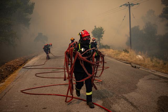 A Greek firefighter holds hoses during a wildfire in the area of Porto Germeno, some 70 kilometres (45 miles) northwest of Athens in the region of Viotia, on August 2, 2026. Greece on August 2, 2026, faced multiple fronts and a growing damage toll after a week of wildfires devastated over 12,000 hectares of forest and agricultural land, experts said. Porto Germeno and other villages were evacuated when the fire broke out on July 31, but local authorities say scores of homes were damaged or destroyed. Hit hard by the climate crisis like the rest of the Mediterranean region, the country is plagued by wildfires every summer due to high temperatures, frequent heat waves, and drought. (Photo by Angelos TZORTZINIS / AFP)