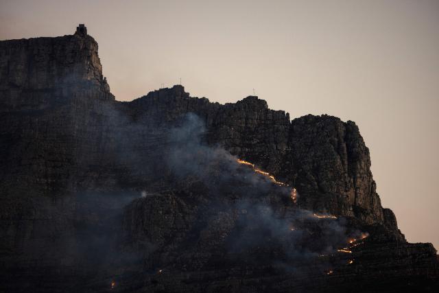 A fire rages on the side of Table Mountain in Cape Town on August 2, 2026. Cape Town firefighters are battling a raging blaze that is moving towards the peak of Table Mountain. (Photo by GIANLUIGI GUERCIA / AFP)