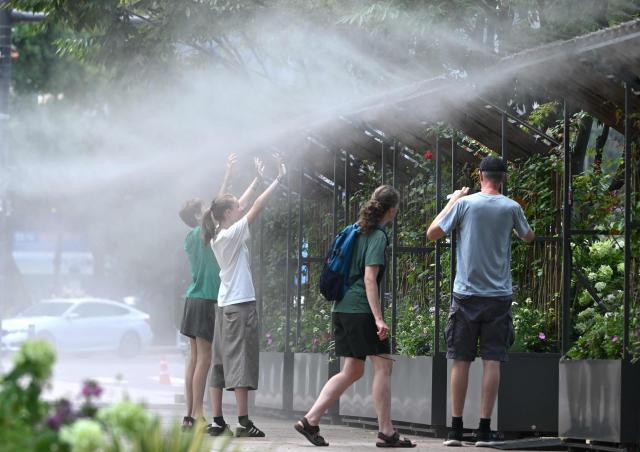 People stand in a mist-spraying zone to cool off on a street in Seoul on August 3, 2026, as a scorching heat wave continues to grip South Korea. South Korea registered its highest temperature since records began more than a century ago on August 2, as authorities warned people to "immediately" stop all outdoor activities in affected areas. (Photo by Jung Yeon-je / AFP)