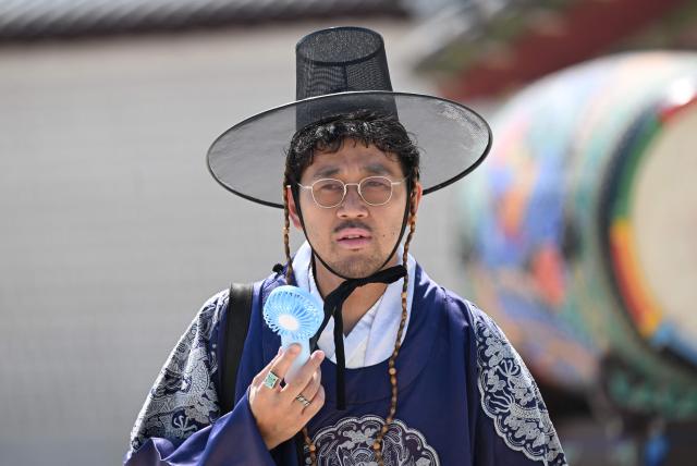 A tourist wearing a traditional Hanbok dress uses a portable fan to cool off at the Gyeongbokgung Palace in Seoul on August 3, 2026, as a scorching heat wave continues to grip South Korea. South Korea registered its highest temperature since records began more than a century ago on August 2, as authorities warned people to "immediately" stop all outdoor activities in affected areas. (Photo by Jung Yeon-je / AFP)