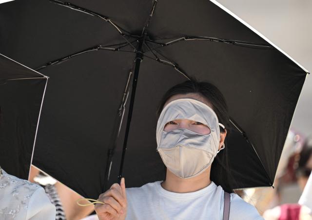 A woman wearing a full-face mask uses a parasol to shield from the sun at the Gyeongbokgung Palace in Seoul on August 3, 2026, as a scorching heat wave continues to grip South Korea. South Korea registered its highest temperature since records began more than a century ago on August 2, as authorities warned people to "immediately" stop all outdoor activities in affected areas. (Photo by Jung Yeon-je / AFP)