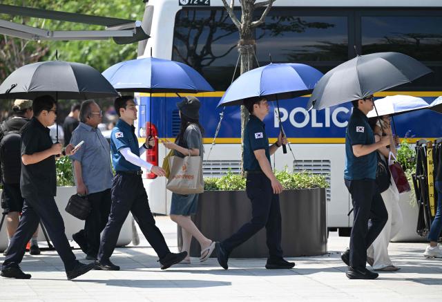 Police officers use umbrellas to shield from the sun on a street in Seoul on August 3, 2026, as a scorching heat wave continues to grip South Korea. South Korea registered its highest temperature since records began more than a century ago on August 2, as authorities warned people to "immediately" stop all outdoor activities in affected areas. (Photo by Jung Yeon-je / AFP)