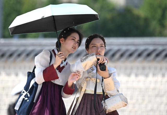 Tourists wearing traditional Hanbok dresses use a parasol to shield from the sun at the Gyeongbokgung Palace in Seoul on August 3, 2026, as a scorching heat wave continues to grip South Korea. South Korea registered its highest temperature since records began more than a century ago on August 2, as authorities warned people to "immediately" stop all outdoor activities in affected areas. (Photo by Jung Yeon-je / AFP)