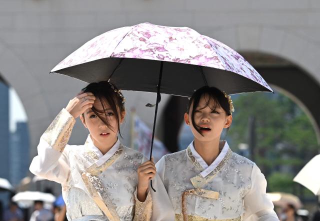 Tourists wearing traditional Hanbok dresses use a parasol to shield from the sun at the Gyeongbokgung Palace in Seoul on August 3, 2026, as a scorching heat wave continues to grip South Korea. South Korea registered its highest temperature since records began more than a century ago on August 2, as authorities warned people to "immediately" stop all outdoor activities in affected areas. (Photo by Jung Yeon-je / AFP)