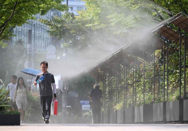 Pedestrians walk along a mist-spraying zone to cool off on a street in Seoul on August 3, 2026, as a scorching heat wave continues to grip South Korea. South Korea registered its highest temperature since records began more than a century ago on August 2, as authorities warned people to "immediately" stop all outdoor activities in affected areas. (Photo by Jung Yeon-je / AFP)