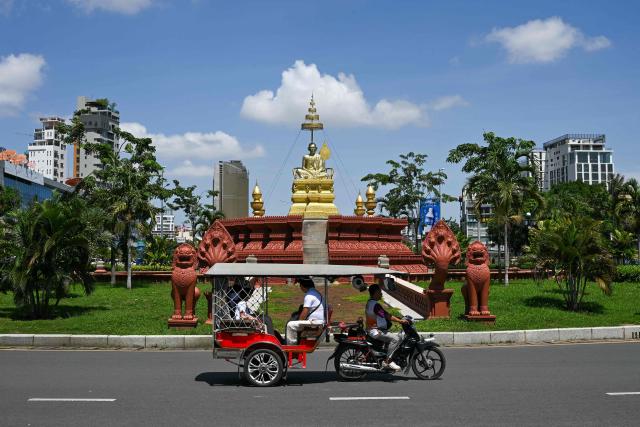 People sit on a tuktuk as they travel past the Samdech Chuon Nath Statue in Phnom Penh on August 3, 2026. (Photo by TANG CHHIN Sothy / AFP)