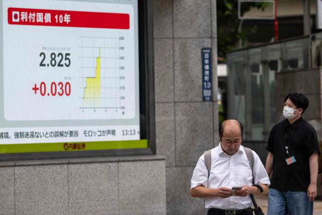 A man checks his phone next to a board showing the figures from the Japanese stock market at a securities firm in Tokyo on August 3, 2026. (Photo by Andrew CABALLERO-REYNOLDS / AFP)