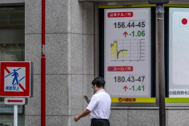 A man checks his phone next to a board showing the US dollar and Japanese yen exchange rate at a securities firm in Tokyo on August 3, 2026. (Photo by Andrew CABALLERO-REYNOLDS / AFP)