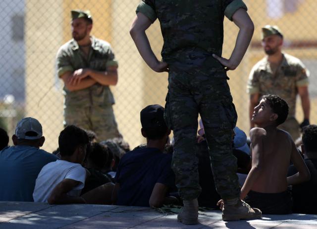 A young migrant looks at a member of the Spanish Army's 'Regulares' infantry force near the border post, prior to escorting them back to Morocco, in the Spanish enclave of Ceuta on August 2, 2026. At least 72 people died during last week's mass influx of migrants into Spain's Ceuta enclave, when tens of thousands of people mostly swam around the border post from Morocco, local officials said today. Most of the estimated 60,000 people who rushed into Spain's north African territory have returned to Morocco since the territory's largest mass migrant crossing. (Photo by Henry NICHOLLS / AFP)