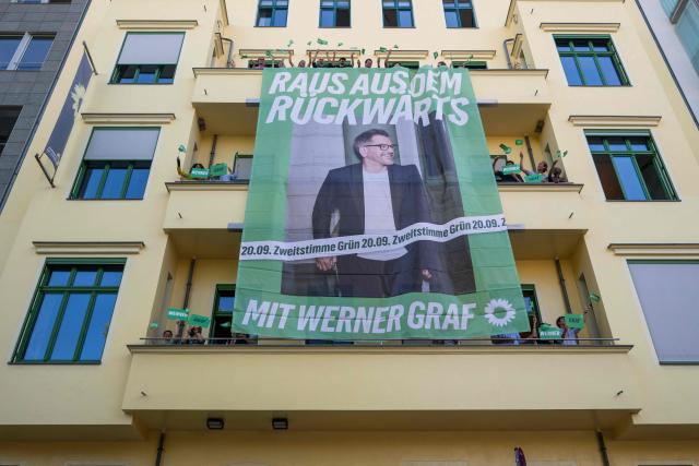Activists of the Green Party wave flags after unfurling a giant election campaign banner featuring the Green Party's main candidate in upcoming regional elections in Berlin Werner Graf on the facade of the Green Party's federal headquarters in Berlin on August 3, 2026. Berlin goes to the polls on September 20, 2026. (Photo by John MACDOUGALL / AFP)