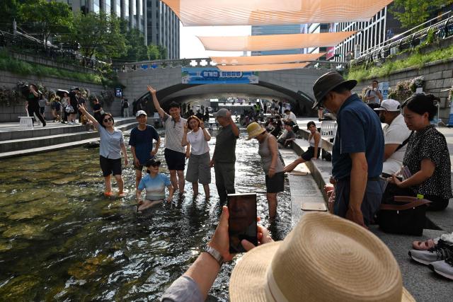 People pose for photos below sunshades over the Cheonggyecheon Stream in Seoul on August 3, 2026. South Korea's weather agency issued a "severe heatwave warning" for Seoul on August 3, the first such advisory since introducing the designation this year to alert the public about increasing extreme temperatures. (Photo by GREG BAKER / AFP)