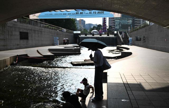 A woman and child shelter from the heat under a bridge over the Cheonggyecheon Stream in Seoul on August 3, 2026. South Korea's weather agency issued a "severe heatwave warning" for Seoul on August 3, the first such advisory since introducing the designation this year to alert the public about increasing extreme temperatures. (Photo by GREG BAKER / AFP)