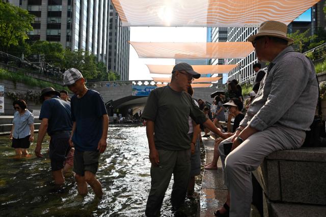 People cool off below sunshades over the Cheonggyecheon Stream in Seoul on August 3, 2026. South Korea's weather agency issued a "severe heatwave warning" for Seoul on August 3, the first such advisory since introducing the designation this year to alert the public about increasing extreme temperatures. (Photo by GREG BAKER / AFP)