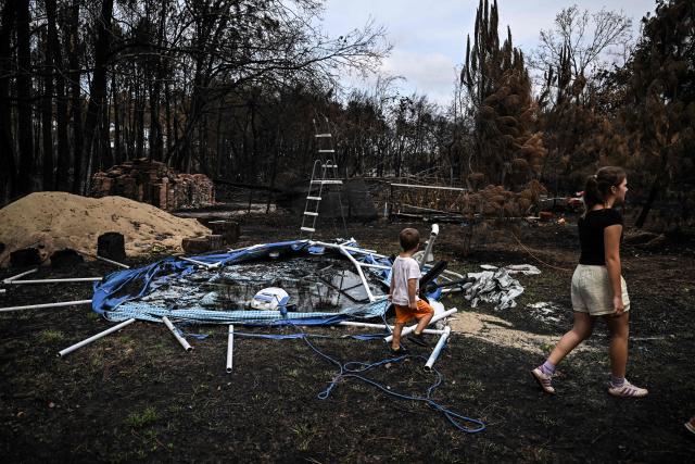 Residents walk past their burnt swimming pool in the garden of his entirely burnt house (unseen) in Le Porge, southwestern France on August 3, 2026, after authorities allowed residents to return to their homes. (Photo by Christophe ARCHAMBAULT / AFP)