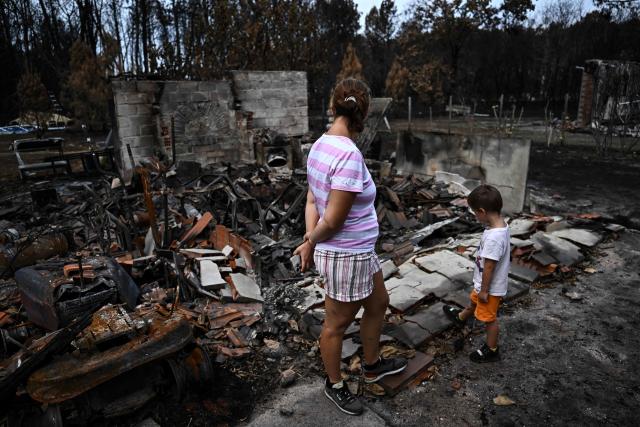 Residents look over burnt debris in the garden of their entirely burnt house (unseen) in Le Porge, southwestern France on August 3, 2006, after authorities allowed residents to return to their homes. (Photo by Christophe ARCHAMBAULT / AFP)