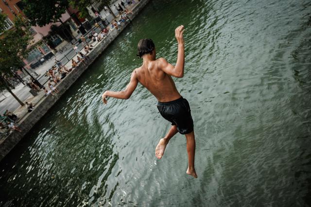 A youth dives into the Canal Saint-Martin in Paris on August 3, 2026. Authorities have stepped up penalties for people swimming outside designated bathing areas or entering the water when a red flag is flying, under a decree published in France's Official Journal that came into force on August 2, 2026. The measure applies nationwide and is intended to strengthen enforcement of coastal and inland water safety rules amid the peak summer holiday season. (Photo by Simon WOHLFAHRT / AFP)