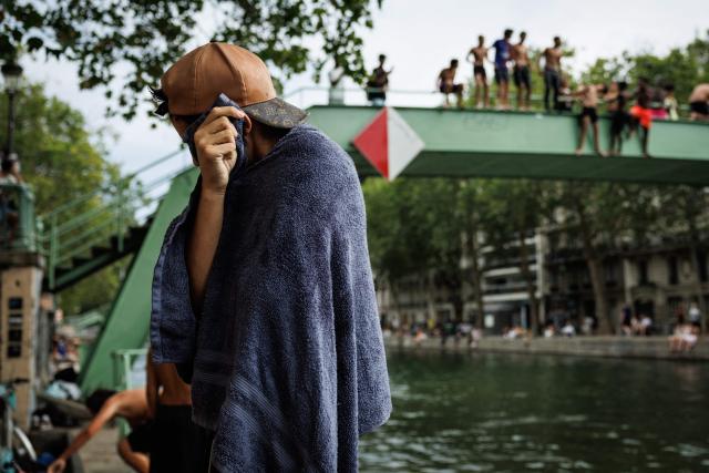 A youth dries up with a towel at the Canal Saint-Martin in Paris on August 3, 2026. Authorities have stepped up penalties for people swimming outside designated bathing areas or entering the water when a red flag is flying, under a decree published in France's Official Journal that came into force on August 2, 2026. The measure applies nationwide and is intended to strengthen enforcement of coastal and inland water safety rules amid the peak summer holiday season. (Photo by Simon WOHLFAHRT / AFP)