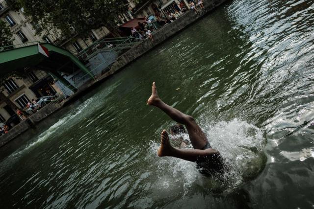 A youth dives into the Canal Saint-Martin in Paris on August 3, 2026. Authorities have stepped up penalties for people swimming outside designated bathing areas or entering the water when a red flag is flying, under a decree published in France's Official Journal that came into force on August 2, 2026. The measure applies nationwide and is intended to strengthen enforcement of coastal and inland water safety rules amid the peak summer holiday season. (Photo by Simon WOHLFAHRT / AFP)