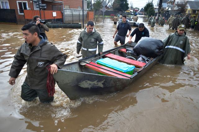 Chilean police officers wade beside their boat in a flooded area of Angol, Araucania region, southern Chile, on August 3, 2026, following heavy rains. (Photo by GUILLERMO SALGADO / AFP)