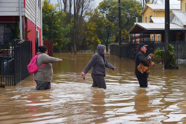People wade in a flooded area of Angol, Araucania region, southern Chile, on August 3, 2026, following heavy rains. (Photo by GUILLERMO SALGADO / AFP)