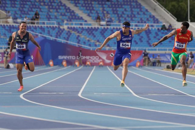 (L to R) Venezuela's Bryant Alamo, Puerto Rico's Eloy Benitez and Grenada's Nazzio John compete in the men's 100m semifinal, heat 2, during the XXV Central American and Caribbean Games at the Felix Sanchez Olympic Stadium in Santo Domingo on August 3, 2026. (Photo by Francesco SPOTORNO / AFP)