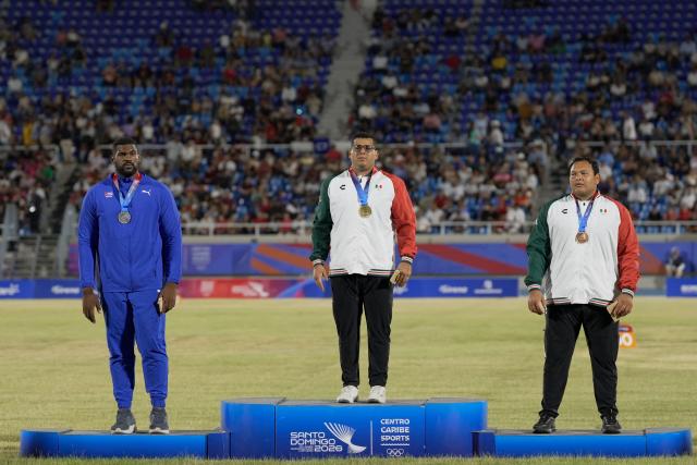 Mexico's Jairo Moran (C), Cuba's Juan Vazquez (L) and Mexico's Uziel Munoz stand on the podium after winning the gold, silver and bronze medals, respectively, in the men's shot put final event during the XXV Central American and Caribbean Games at the Felix Sanchez Olympic Stadium in Santo Domingo on August 3, 2026. (Photo by Francesco SPOTORNO / AFP)