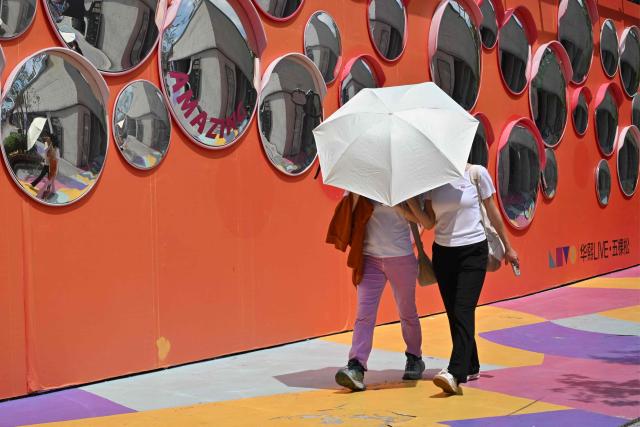 Women use an umbrella to protect from the sun as they visit a shopping mall in Beijing on August 4, 2026. (Photo by ADEK BERRY / AFP)