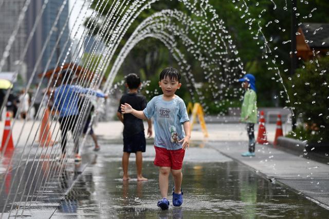 A child cools off in a fountain in Seoul on August 4, 2026. South Korea's summer heat has killed 16 people so far this year, the interior ministry said August 4, as the nation swelters in a wave of searing weather. (Photo by GREG BAKER / AFP)