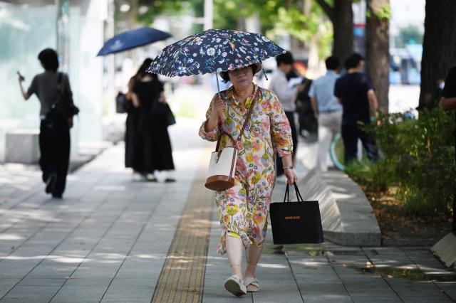 A woman shelters from the heat under an umbrella in Seoul on August 4, 2026. South Korea's summer heat has killed 16 people so far this year, the interior ministry said August 4, as the nation swelters in a wave of searing weather. (Photo by GREG BAKER / AFP)