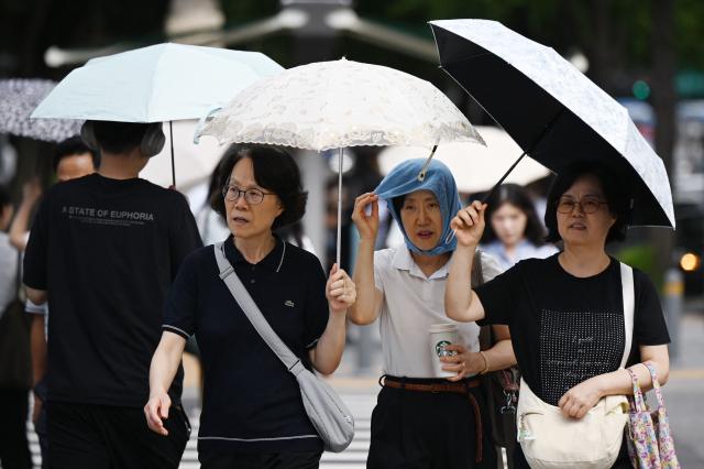 People shelter from the heat under umbrellas in Seoul on August 4, 2026. South Korea's summer heat has killed 16 people so far this year, the interior ministry said August 4, as the nation swelters in a wave of searing weather. (Photo by GREG BAKER / AFP)