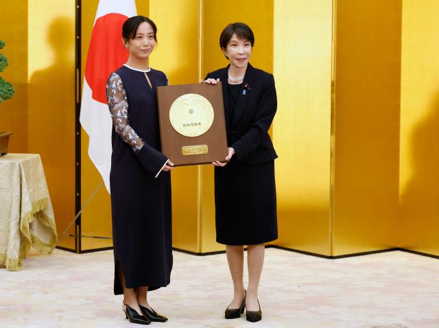 Japanese Prime Minister Sanae Takaichi (R) and speed skater Miho Takagi pose with the People's Honor Award plaque during a ceremony at the prime minister's office in Tokyo on August 4, 2026. (Photo by Franck ROBICHON / POOL / AFP)