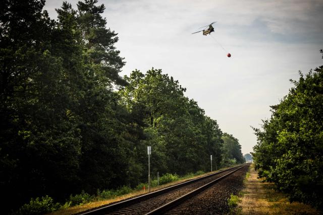 A Royal Netherlands Air Force CH-47 Chinook helicopter carries a load of water as firefighters operate to extinguish a wildfire sweeping through the Boschhuizerbergen nature reserve near Oostrum, in the Dutch municipality of Venray, south-eastern Netherlands on August 4, 2026. (Photo by ROB ENGELAAR / ANP / AFP) / Netherlands OUT