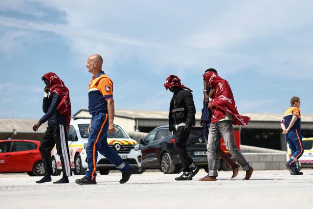Migrants walk with a member of France's Civil Defence after disembarking from a French rescue ship following their rescue at sea after their boat caught fire during an attempt to cross the English Channel from France to Britain, at the Port de Commerce in Boulogne-sur-Mer, northern France, on August 4, 2026. French and British vessels saved 157 migrants after their boat caught fire while trying to cross the Channel on August 4, authorities in both countries said. It is one of the largest such rescue operations reported since records began in 2018. (Photo by Sameer AL-DOUMY / AFP)