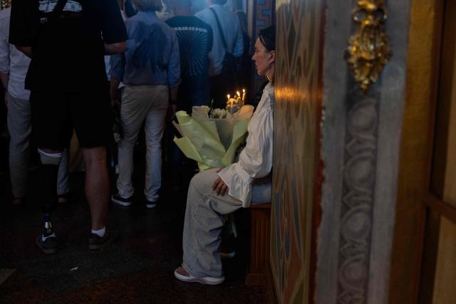 A relative sits with a bunch of flowers during the funeral ceremony of Vitalina "Frau" Yarovenko, a 20-year-old volunteer and activist who was killed in a Russian attack that killed 9 people on August 1, at the Saint Michael's Golden-Domed Monastery in Kyiv on August 4, 2026, amid the Russian invasion of Ukraine. (Photo by Tetiana DZHAFAROVA / AFP)