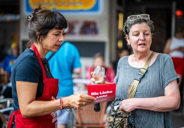 The Left Party's (Die Linke) main candidate in upcoming regional elections in Berlin Elif Eralp (L) hands out a leaflet at a cafe during a campaign stop in Berlin's Schoeneberg district on August 4, 2026. Berlin goes to the polls on September 20, 2026. (Photo by John MACDOUGALL / AFP)