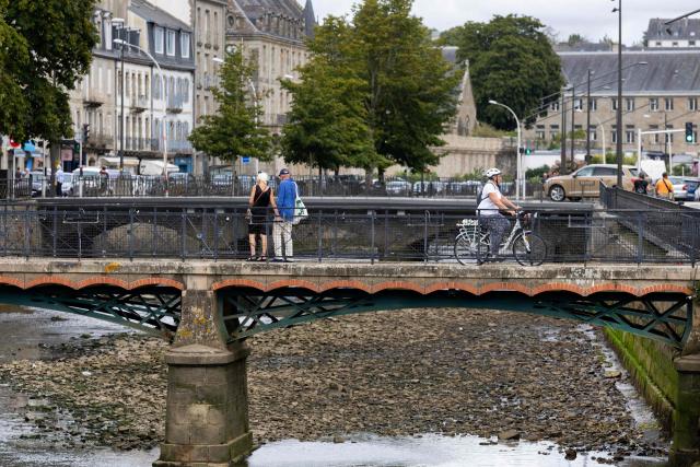 Two people look from a bridge at the dried-out riverbed of the Odet River in Quimper, north-western France on August 4, 2026, as a heatwave hits France. The basin of the Odet river faces a "drought crisis," according to the Finistère prefecture. (Photo by Fred TANNEAU / AFP)