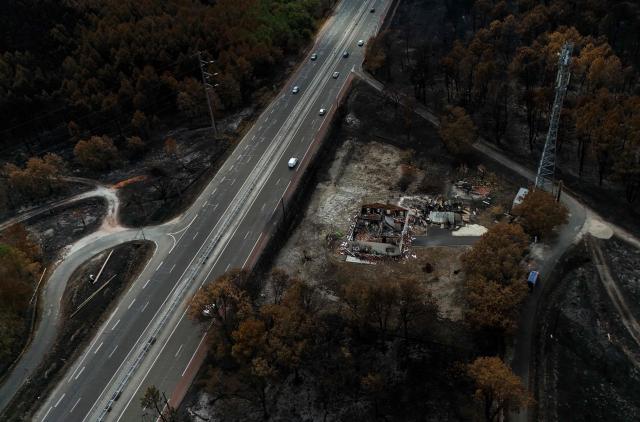 This aerial photograph shows cars driving down a road next to a burnt property in the wake of a wildfire that swept through the Gironde region in Lanton, along the Arcachon bay, southwestern France on August 4, 2026. (Photo by Christophe ARCHAMBAULT / AFP)