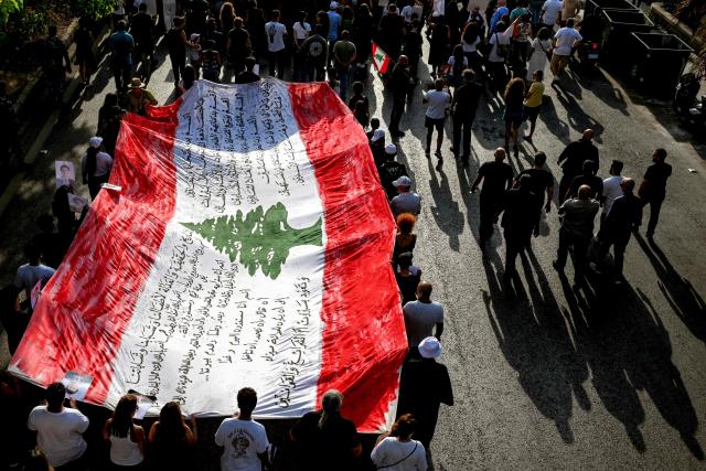 Family members and relatives of the victims of the 2020 Beirut port explosion march with a giant Lebanese flag on the sixth anniversary of the incident near the port area in Beirut on August 4, 2026. The massive Beirut port explosion on August 4, 2020, killed more than 220 people, injured more that 6,500 and damaged swathes of the capital. Lebanese authorities have said the explosion was triggered by a fire in a warehouse where tonnes of ammonium nitrate fertiliser had been stored haphazardly for years, despite repeated warnings to senior officials. (Photo by Joseph EID / AFP)