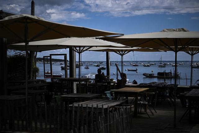 Tourists sit at the terrasse of a freshly-reopened restaurant after authorities allowed people back on the Cap Ferret peninsula in the wake of the wildfire which engulfed the Gironde region in Lege-Cap-Ferret, along the Arcachon bay, southwestern France on August 4, 2006. (Photo by Christophe ARCHAMBAULT / AFP)
