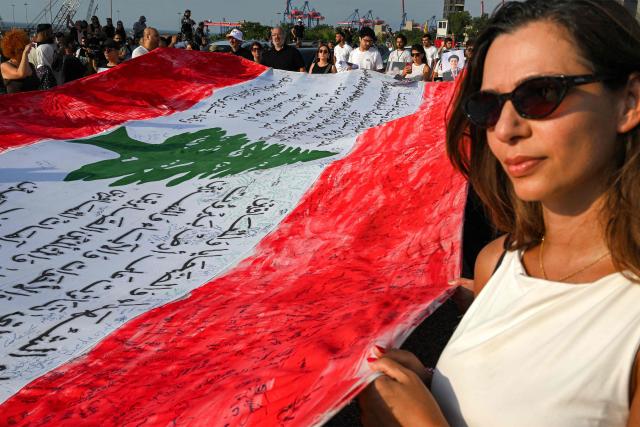 Family members and relatives of the victims of the 2020 Beirut port explosion march with a giant Lebanese flag on the sixth anniversary of the incident near the port area in Beirut on August 4, 2026. The massive Beirut port explosion on August 4, 2020, killed more than 220 people, injured more that 6,500 and damaged swathes of the capital. Lebanese authorities have said the explosion was triggered by a fire in a warehouse where tonnes of ammonium nitrate fertiliser had been stored haphazardly for years, despite repeated warnings to senior officials. (Photo by Joseph EID / AFP)
